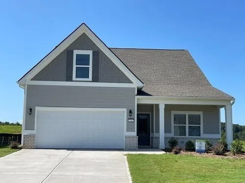 Modern gray single-family home with a two-car garage, front porch, and manicured lawn under clear blue sky.